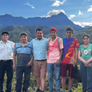 Six coffee producers and farmers standing together outdoors in front of a mountain range under a blue sky with clouds.
