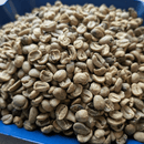 A close-up pile of raw, unroasted coffee beans in a light tan and green color, filling a blue container.
